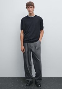 Black short-sleeve sweater with a crew neck, paired with gray tailored trousers and black shoes. Smooth texture, relaxed fit.