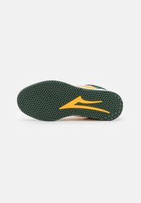 Athletic shoe sole with dark green hexagonal tread pattern and central yellow stylized logo on a white background.