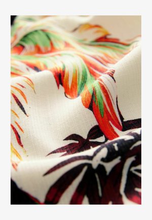 Tissu avec un fond crème orné de motifs floraux éclatants en orange, vert et marron foncé. Texture lisse avec un léger éclat.
