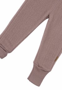 Fleece teplákové nohavice v mäkkej broskyňovej farbe so žebrovanými manžetami. Majú hladkú textúru a malú značkovú nášivku na spodnej časti nohy.
