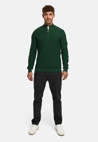 Grøn striktrøje med høj krave og kvart lynlås design, parret med sorte jeans og hvide sneakers, med en struktureret stof.