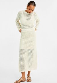 Gebreid twee-delig outfit in off-white, met een gestreept bovenstuk met lange mouwen en een maxi rok, ontworpen met diamantvormige uitsparingen.