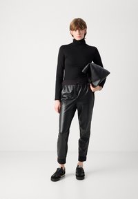 Black turtleneck top, glossy black jogger pants with an elastic waistband, and black sneakers. The model holds a textured black clutch.