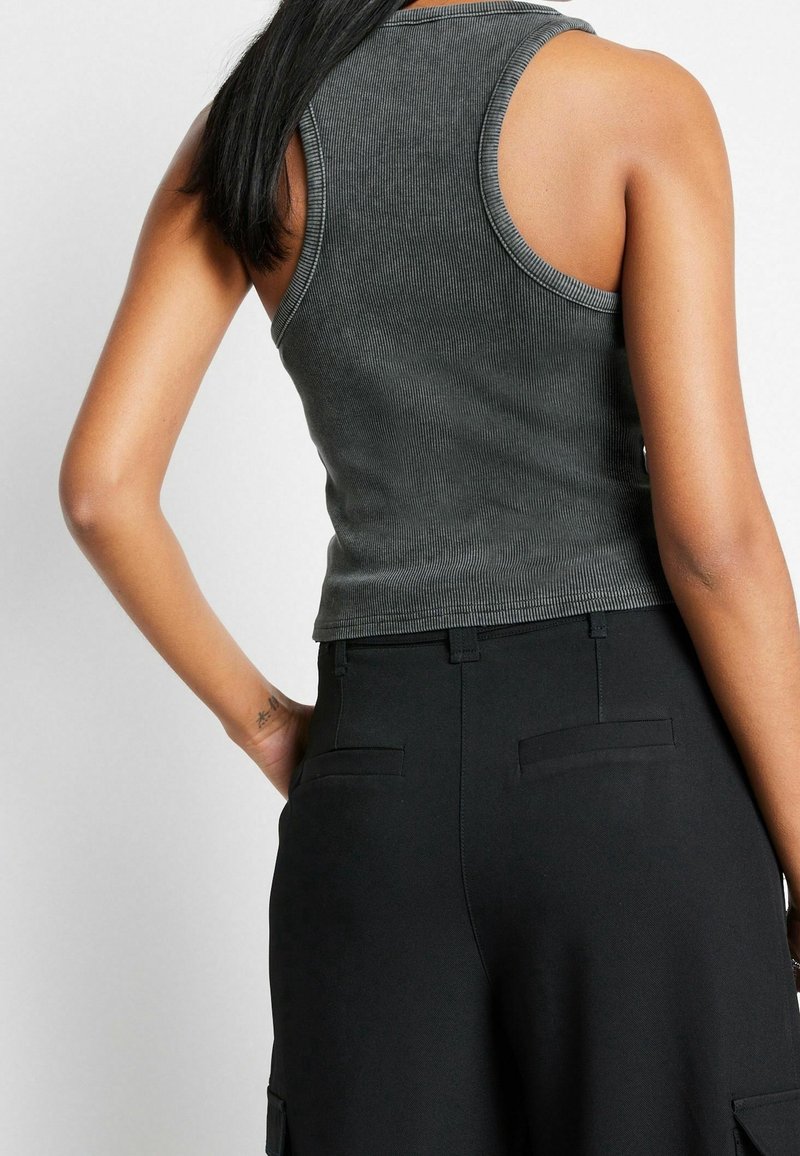 Top de tirantes gris con relieve, con escote redondo y diseño sin mangas, combinado con pantalones negros de cintura alta con bolsillos laterales.