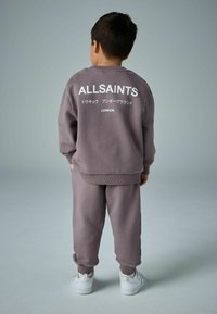 Pelēks džemperis ar baltu "ALLSAINTS" uzrakstu, saskaņots ar atbilstošām sporta biksēm un baltām kedām. Mīksta auduma, brīvs piegriezums, ribota piedurkne.
