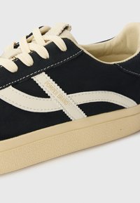 Basket en suede noir avec semelle en caoutchouc blanche, rayures latérales blanches contrastantes et lacets crème. Logo "Pompeii Brand" en doré sur le côté.