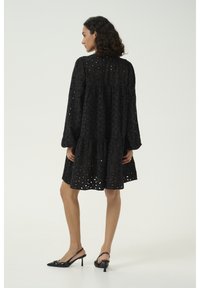 Svart ögla klänning med långa ärmar, lagerdesign och intrikata blommig utskärningar. Matchad med svarta slingback-hälar med spetsiga tår.
