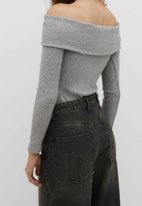 Femme portant un haut gris côtelé à épaules dénudées et un jean noir délavé taille haute, vue de dos et de côté.