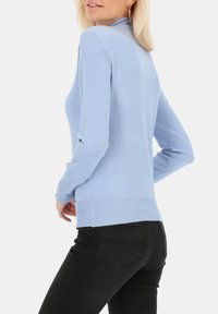Jasnoniebieski sweter z długim rękawem i wysokim kołnierzem, z prążkowanym wykończeniem u dołu i przy mankietach, w połączeniu z czarnymi, dopasowanymi dżinsami. Gładka tekstura i dopasowany krój.