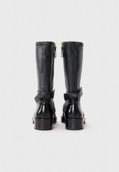 Czarne skórzane kozaki do kolan z zamkami błyskawicznymi, kokardkami przy kostce i masywnym obcasem. Gładka faktura z błyszczącym wykończeniem.