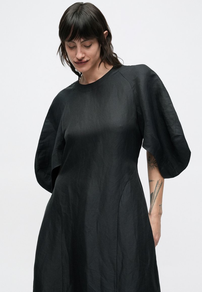 Vestito nero con vestibilità morbida, scollo arrotondato e maniche corte a sbuffo. Realizzato in tessuto leggero con una sottile lucentezza.