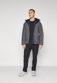 Gray waterproof jacket with a hood, featuring a front zipper and pockets, paired with black pants and light gray sneakers.
