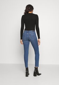 Top negro de manga larga acanalado combinado con jeans de mezclilla azules ajustados. Los jeans tienen bolsillos traseros y se llevan con botas de tacón negras hasta el tobillo.