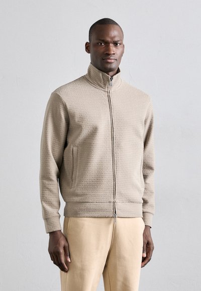 Giacca zip-up beige chiaro realizzata in materiale testurizzato, con colletto alto, tasche laterali e polsini e orlo a costine.
