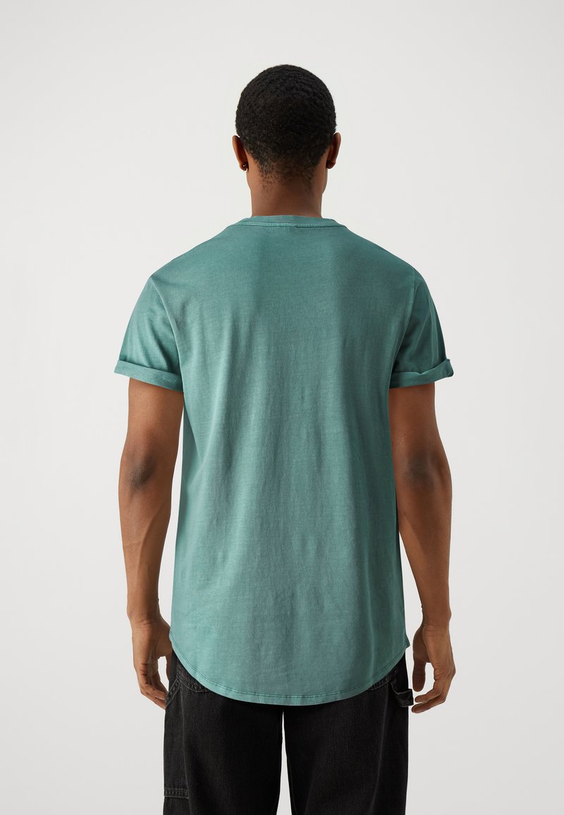 Helles türkisfarbenes T-Shirt mit kurzen Ärmeln und umgeschlagenen Ärmeln, runder Ausschnitt und leicht abgerundetem Saum, aus weichem, strukturiertem Stoff.