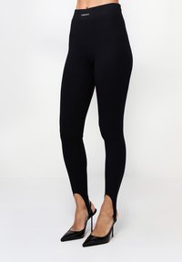 Fekete leggings, magas derékkal, oldalsó hasítékokkal a bokáknál. Rugalmas anyagból készült, hogy kényelmet és mozgásszabadságot biztosítson.