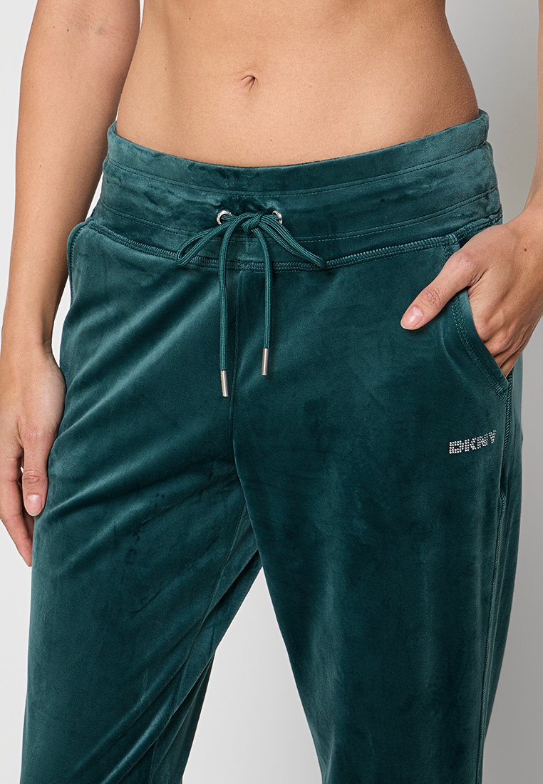 Kobiece tors z założonymi zielonymi welurowymi spodniami dresowymi z kieszenią po prawej stronie, prezentujące odsłonięty brzuch i pępek.