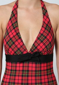 Maillot de bain à carreaux rouges avec un design plongeant en V, taille noire avec un accent nœud, présentant une texture lisse et des couleurs vives.