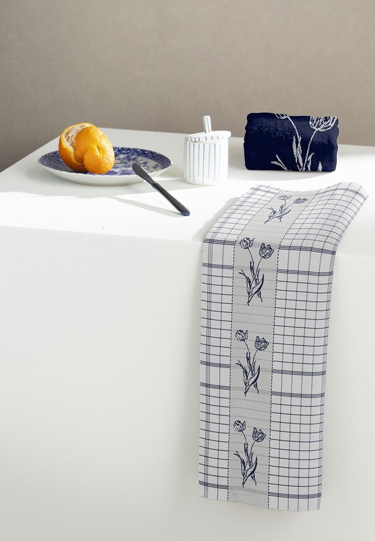 Bawełniany obrus w biało-granatową kratkę, ozdobiony haftowanymi tulipanami. Towarzyszy mu niebieski talerz, chleb i biały cukierniczek.