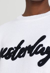 Biały dzianinowy sweter z napisem „yesterday” w grubych czarnych literach na piersi. Wykończenie ze ściągaczem przy dekolcie i miękka faktura.