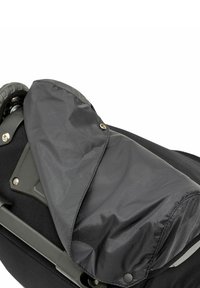 Borsa in tessuto nero con finitura opaca, dotata di una patta pieghevole fissata da bottoni a pressione e hardware visibile, posizionata su un telaio con ruote.
