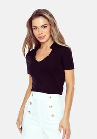 Czarna koszulka z dekoltem w serek, krótki rękaw, wykonana z gładkiego materiału, w zestawie z białymi spodniami o wysokim stanie z złotymi guzikami jako akcenty.