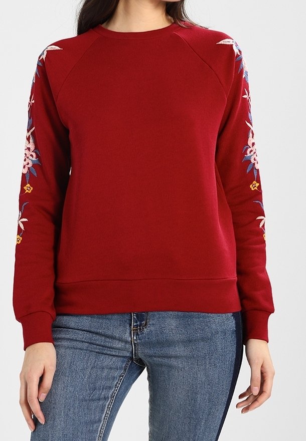 Sudadera color carmesí con mangas raglán, con bordado floral en rosa, azul y amarillo en los hombros. Mezcla de algodón, ajuste casual.