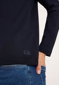 Navy lange mouwen shirt met een slim fit ontwerp en een gestructureerde stof. Beschikt over een subtiele logo-detail aan de onderrand en is gecombineerd met blauwe denim.