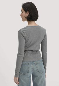 Graues Langarmoberteil mit weitem Halsausschnitt, texturiertem Stoff und einer geknoteten Taille, kombiniert mit hellen gerade geschnittenen Jeans.