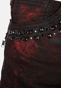 Tessuto in denim nero con un motivo astratto rosso, caratterizzato da una fila di borchie a piramide nere e accenti circolari lungo la vita.