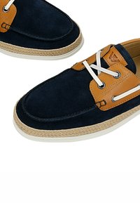 Chaussures bateau en daim bleu marine avec accents en cuir marron clair, lacets blancs, bordure en corde tressée et semelles en caoutchouc blanc.