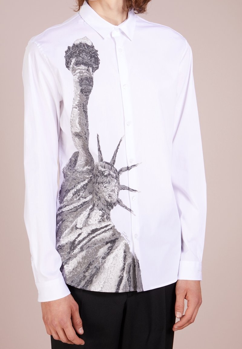 Camisa blanca con una ilustración en escala de grises de la Estatua de la Libertad en un lado, con botones y un cuello clásico.