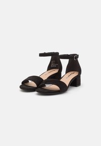 Zwarte suède sandalen met hak, gesloten achterkant, enkelbandje, open teen ontwerp en een lage blokhak. Glad binnenvoering met minimale branding.