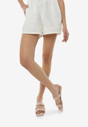 Beige schuifsandalen met twee brede banden en een gladde textuur. Gecombineerd met witte linnen shorts, die een relaxte pasvorm en een casual stijl laten zien.