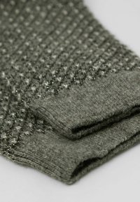 Pull en laine vert tricoté avec un motif texturé et des mailles en relief, des poignets repliés et une finition douce.