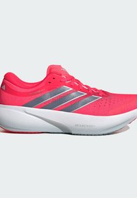 Chaussure de course Adidas Supernova rose vif avec semelle blanche épaisse et bandes argentées, équipée de la technologie d'amorti Dreamstrike+.