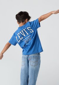 Modrá bavlněná tričko s potiskem "LEVI'S" a "THE ORIGINAL 1873" na zadní straně v bílé barvě. V kombinaci se světle modrými džíny.