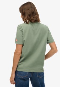 Groen katoenen t-shirt met korte mouwen, ronde hals en een klein merklijntje op de linkermouw. Gecombineerd met blauwe spijkerbroek.