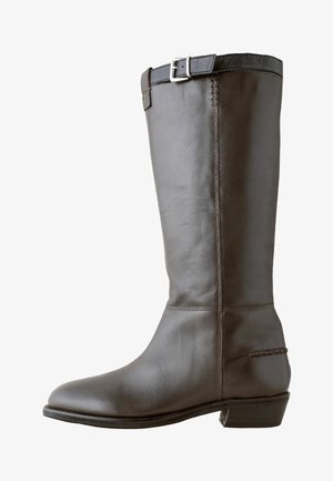 Hnedá kožená jazdecká čižma s okrúhlou špičkou, vysokým zvrškom a dekoratívnou prackou na hornej strane. Obsahuje prešité detaily a nízky podpätok.