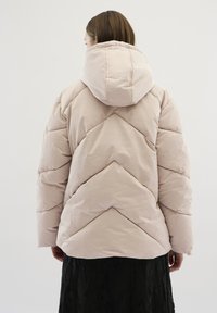 Gevoerde roze jas met capuchon, voorzien van een chevron-quiltpatroon. Zacht, lichtgewicht materiaal biedt warmte en een relaxte pasvorm.