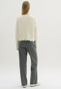 Weißer gerippter Pullover mit ausgefranstem Saum und langen Ärmeln, kombiniert mit grauen Nadelstreifen-Hosen und cremefarbenen Ballerinas. Rückansicht.