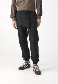 Svarta joggers i lätt material, med dragsko i midjan, sidofickor med dragkedja och elastiska mudd. Kombinerat med vinröda sneakers.