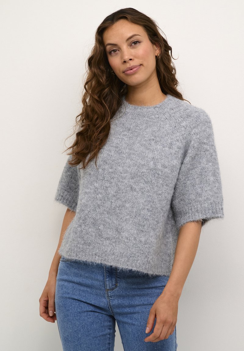 Light gray, short-sleeved sweater made of fluffy material, featuring a round neckline and a relaxed fit; worn with blue jeans.