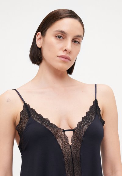 Black sleepwear with lace detailing along the neckline and adjustable spaghetti straps. Soft texture and relaxed fit accentuate the silhouette.