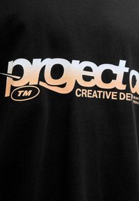 Zwarte t-shirt met grote witte en lichtoranje tekst. Het ontwerp leest "project" met een spiraal en "CREATIVE DEP." eronder, voornamelijk gedrukt op de voorkant.
