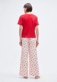 T-shirt en coton rouge associé à un pantalon large ecru orné d'un motif de cerises rouges et vertes, avec une texture douce et une coupe décontractée.