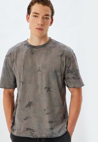 Grå tie-dye T-shirt med korte ærmer, rund halsudskæring og en blød tekstur. Stoffet viser en blanding af mørke og lyse grå mønstre.