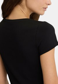 T-shirt nera aderente con maniche corte, realizzata in morbido cotone, scollatura arrotondata e dettagli di cucitura discreti lungo l'orlo.
