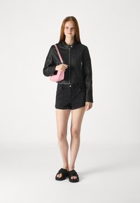 Giacca cropped in pelle nera con chiusura zip, abbinata a pantaloni corti neri a vita alta e sandali neri. Accessoriata con una borsa a tracolla rosa.