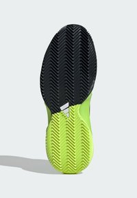 Suela de zapato deportivo con un diseño de goma negra texturizada y verde brillante. Presenta un patrón de tracción en espiga y un distintivo detalle de logo en blanco.